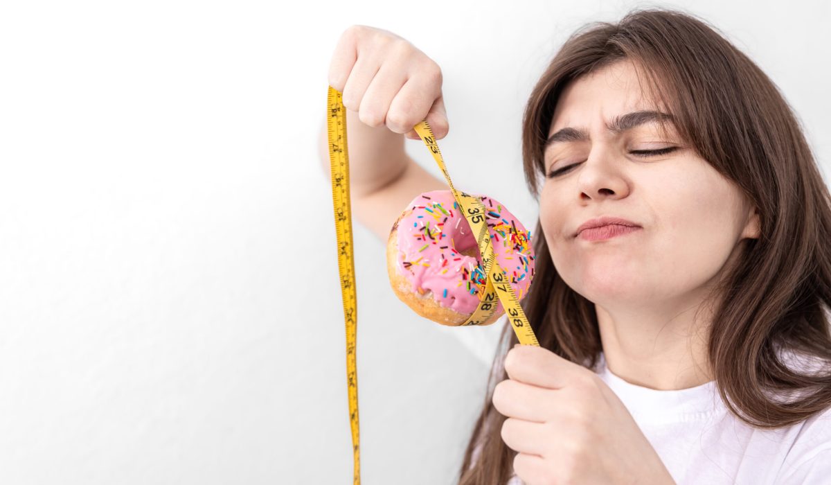 Young woman holding donut with measuring tape, concept of diet, calorie food, overeating, weight gain set.